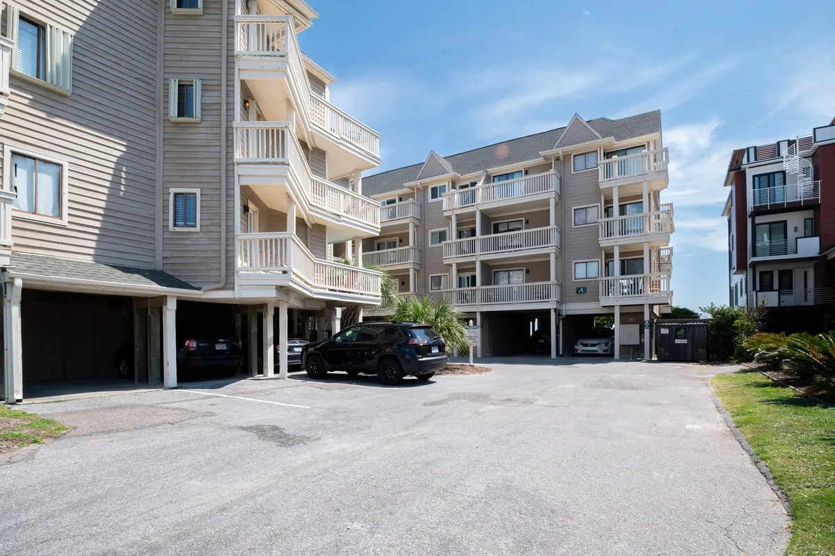 An exterior view of multi-story condo buildings framed by palm trees, with a clear parking area in front. The sunny, inviting atmosphere hints at the proximity to the beach and local attractions, while the palm trees evoke a classic coastal vibe. The openness visually suggests easy access to outdoor adventures and neighborhood exploration.
