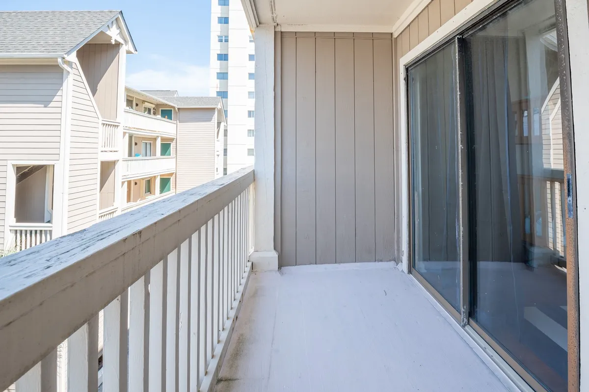 A tranquil balcony space is shown with a sturdy railing, sliding glass doors, and the building's exterior siding. It's an inviting spot designed for relaxation, reading, or enjoying a morning coffee while overlooking the surroundings.