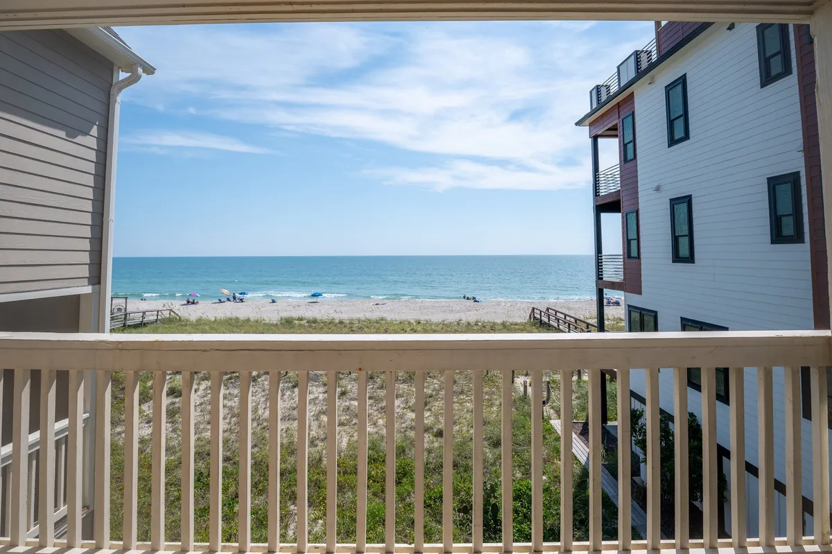 Taken from a balcony, this image frames a panoramic view of the sandy beach, ocean, and open sky. The inviting scene captures people engaging in classic coastal activities, like sunbathing and strolling, and emphasizes the tranquil seaside atmosphere.