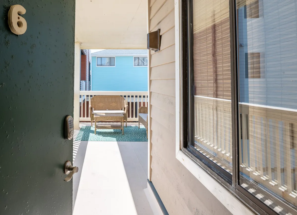 A cozy patio area featuring a green door, wicker chair, and sunlit patio space. This inviting nook is ideal for relaxing after a day of exploration. The scene suggests the simple pleasures of enjoying fresh air, morning coffee, or evening conversations while soaking up the natural ambiance.