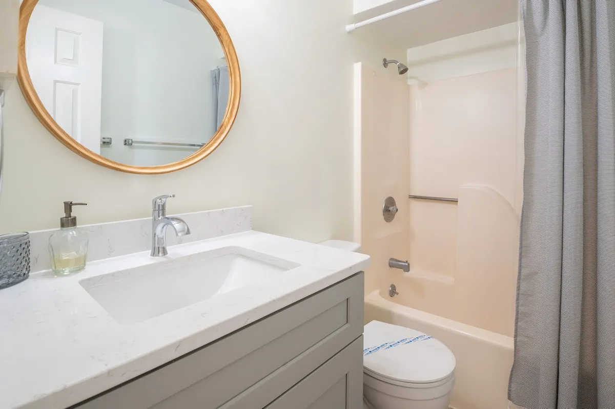 A stylish, modern bathroom with a large round mirror above a sleek vanity and a glass-enclosed shower area. The space feels bright and refreshing, with clean lines and minimal decor creating a spa-like vibe.