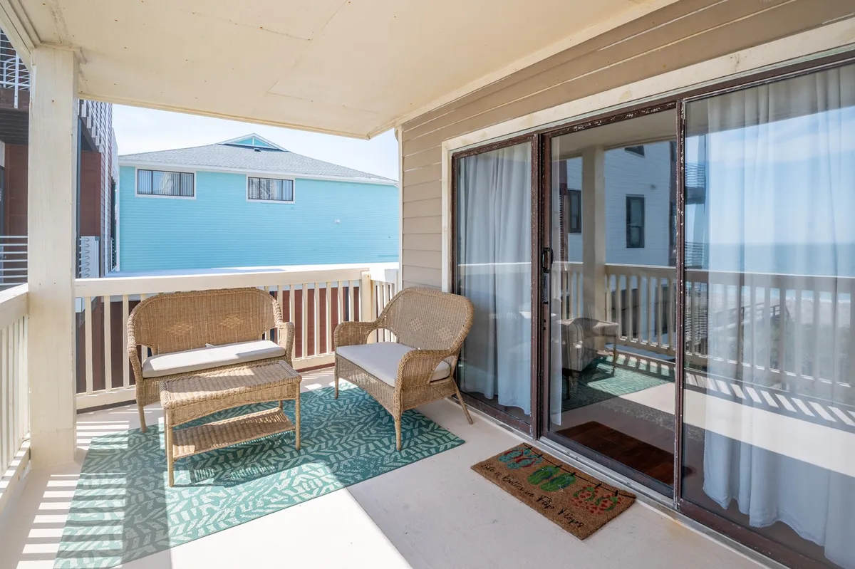 A tranquil porch scene featuring wicker chairs and a green patterned rug set against a backdrop of breathtaking ocean views. The sliding glass door links this space to the living area, reinforcing the indoor-outdoor connection. The porch exudes relaxation and invites moments of sunrise coffee or sunset cocktails.